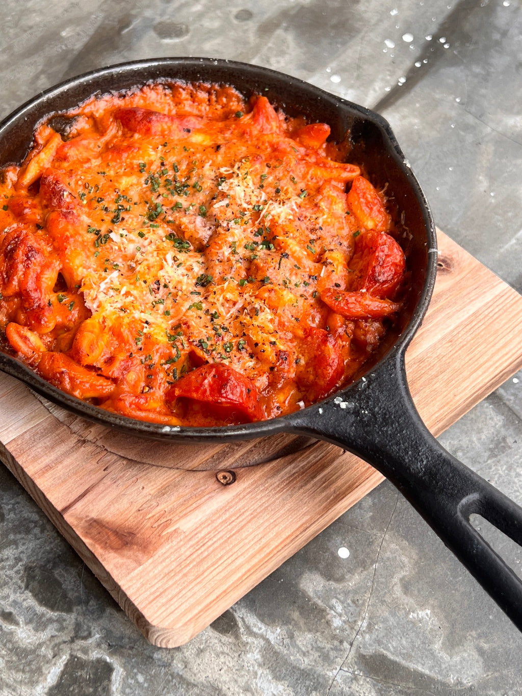 Cast iron skillet with baked dish on a wooden board over a gray marble background