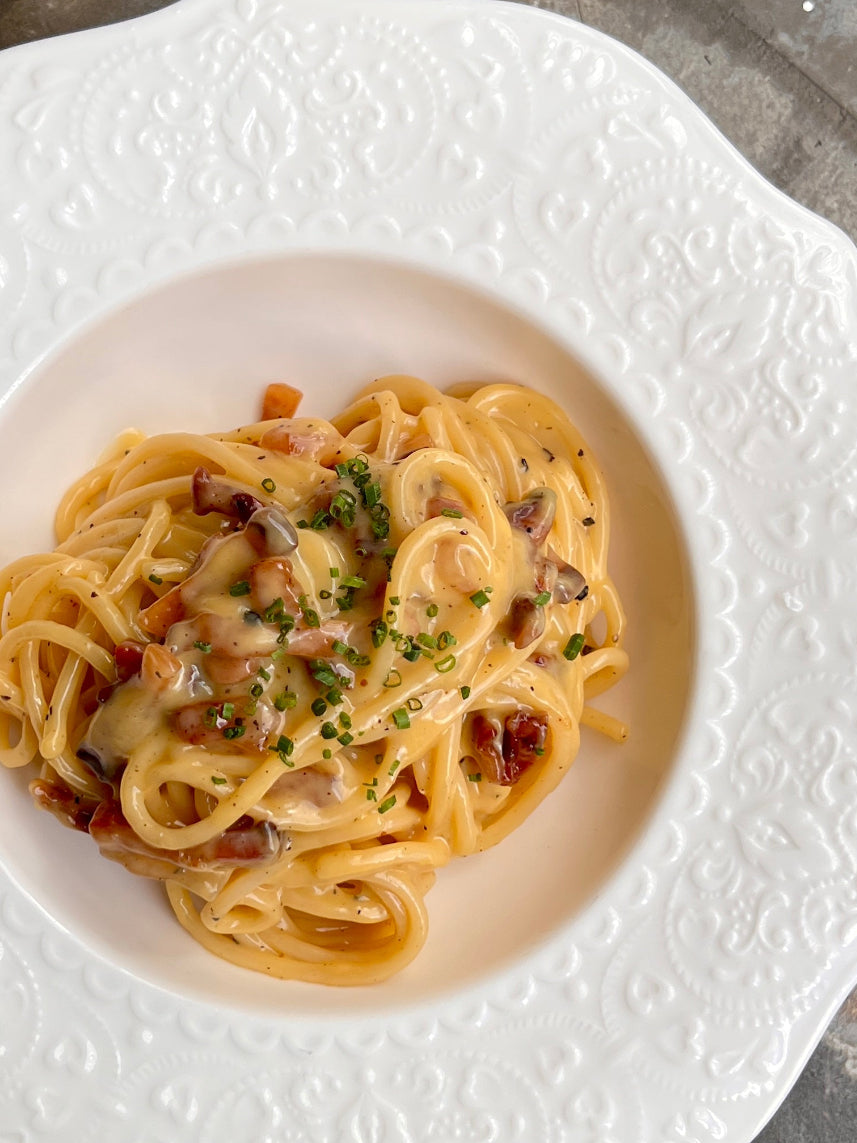 White bowl with carbonara pasta on a textured stone surface