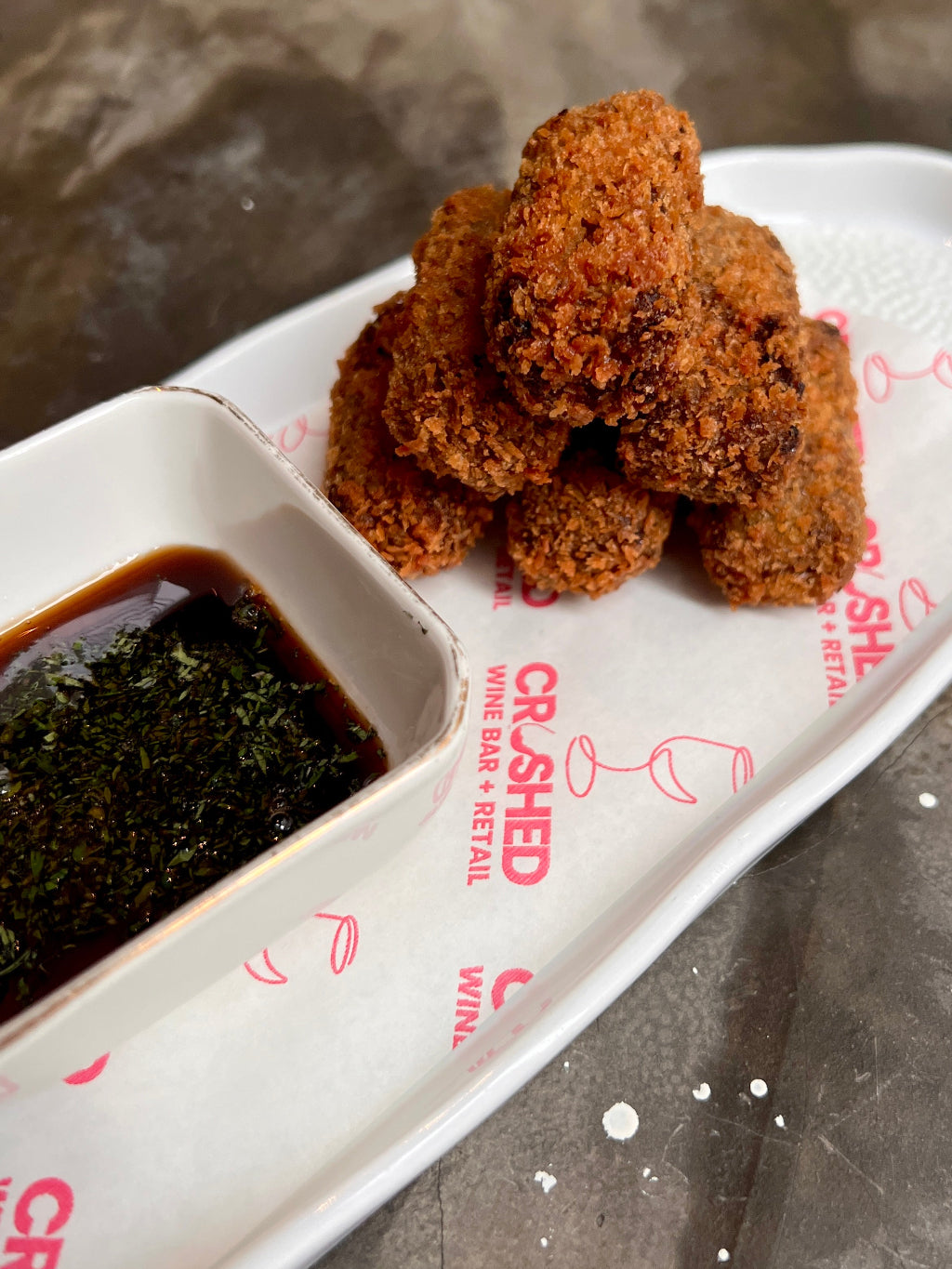 White plate with crumbed lamb croquettes and a small ramekin of dark malt vinegar reduction with mint