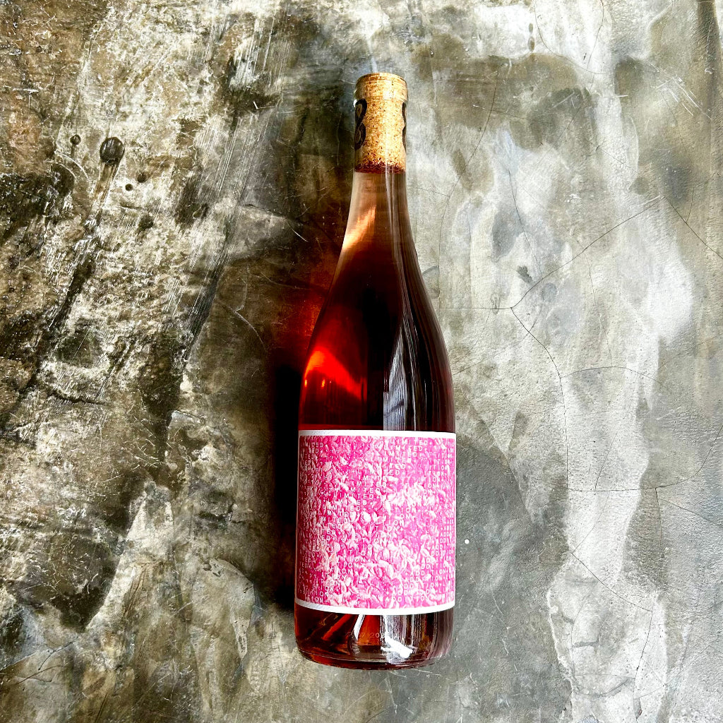 Bottle of rose wine with a pink label on a textured stone surface